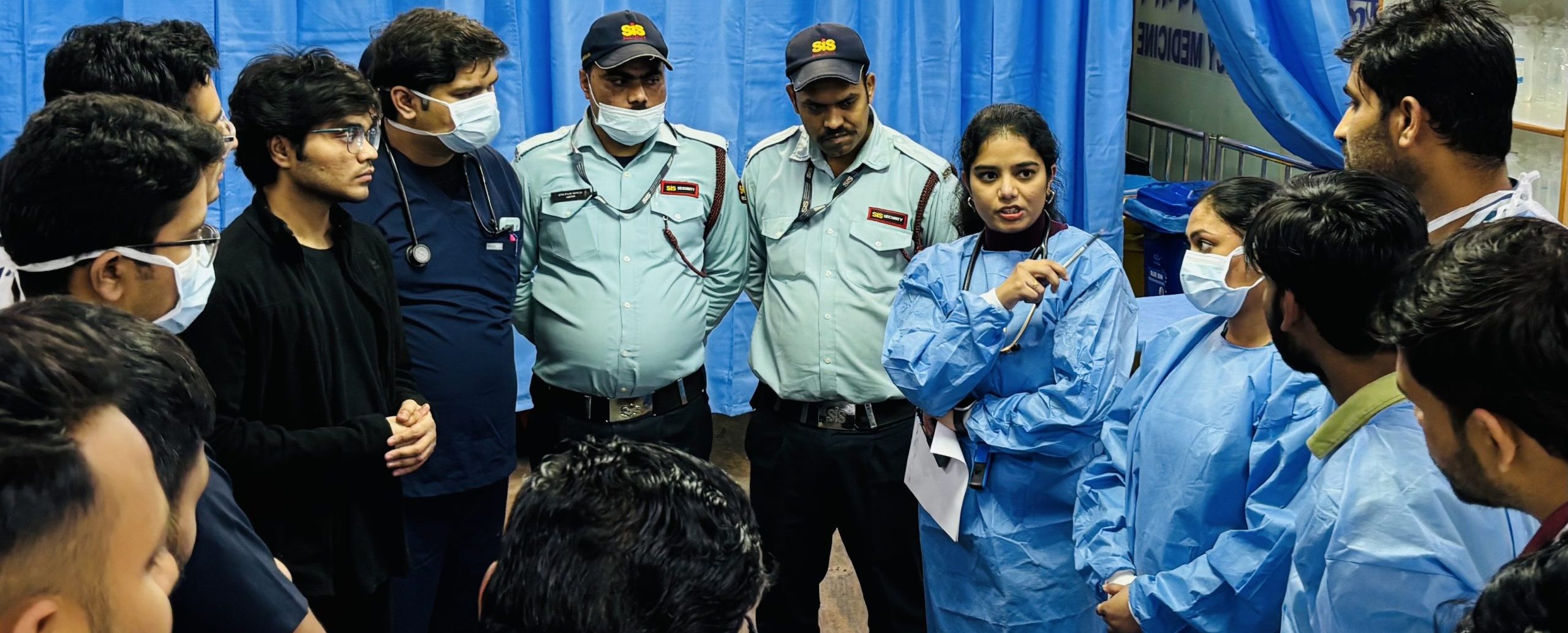 Emergency Department staff standing together in a bright clinical area, wearing scrubs and PPE, preparing for a shift‑start discussion.