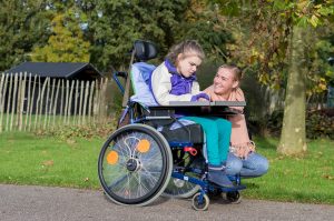 Disabled child in wheelchair relaxing outside together with a care assistant